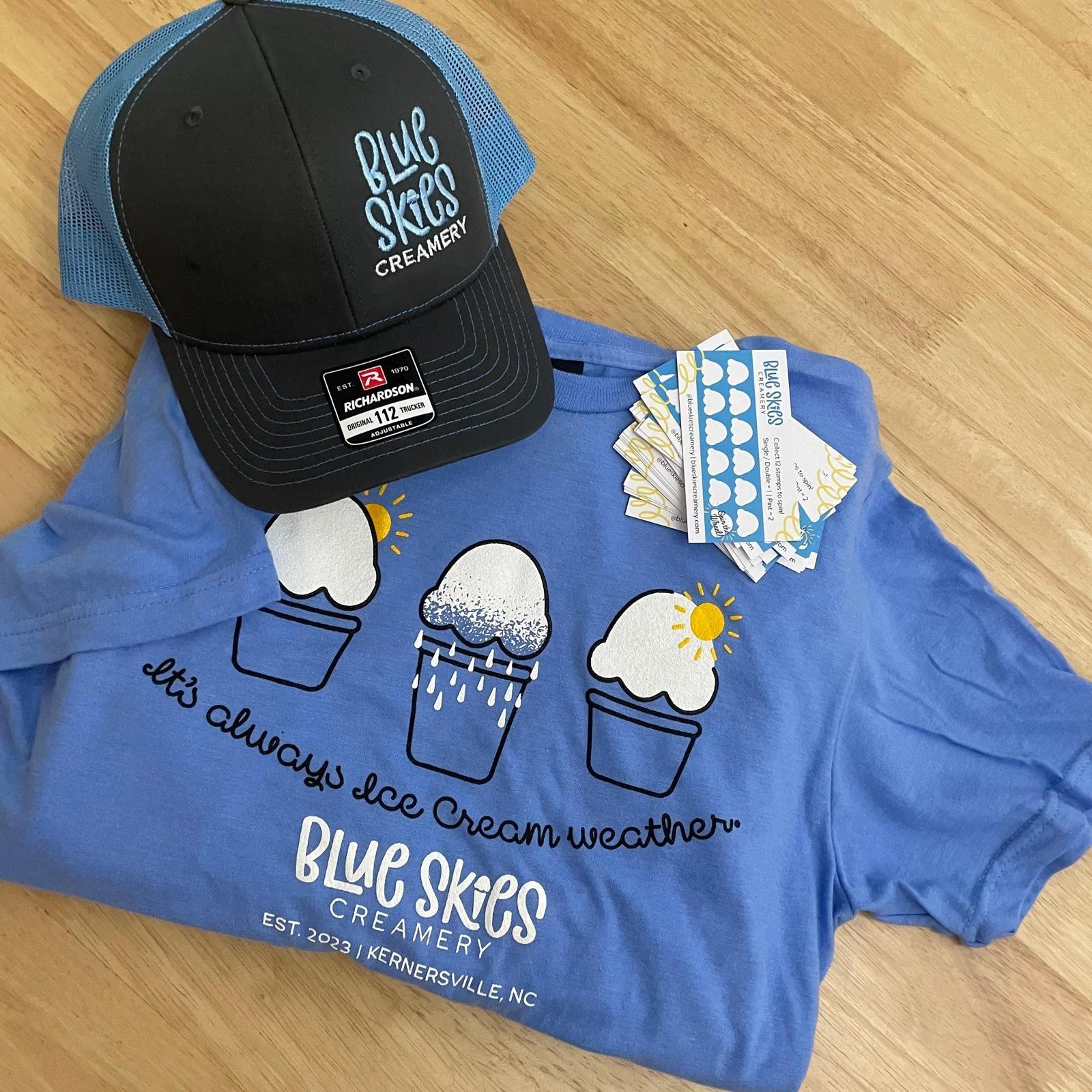 Blue Skies Creamery t-shirt and hat with ice cream graphics on a wooden surface.