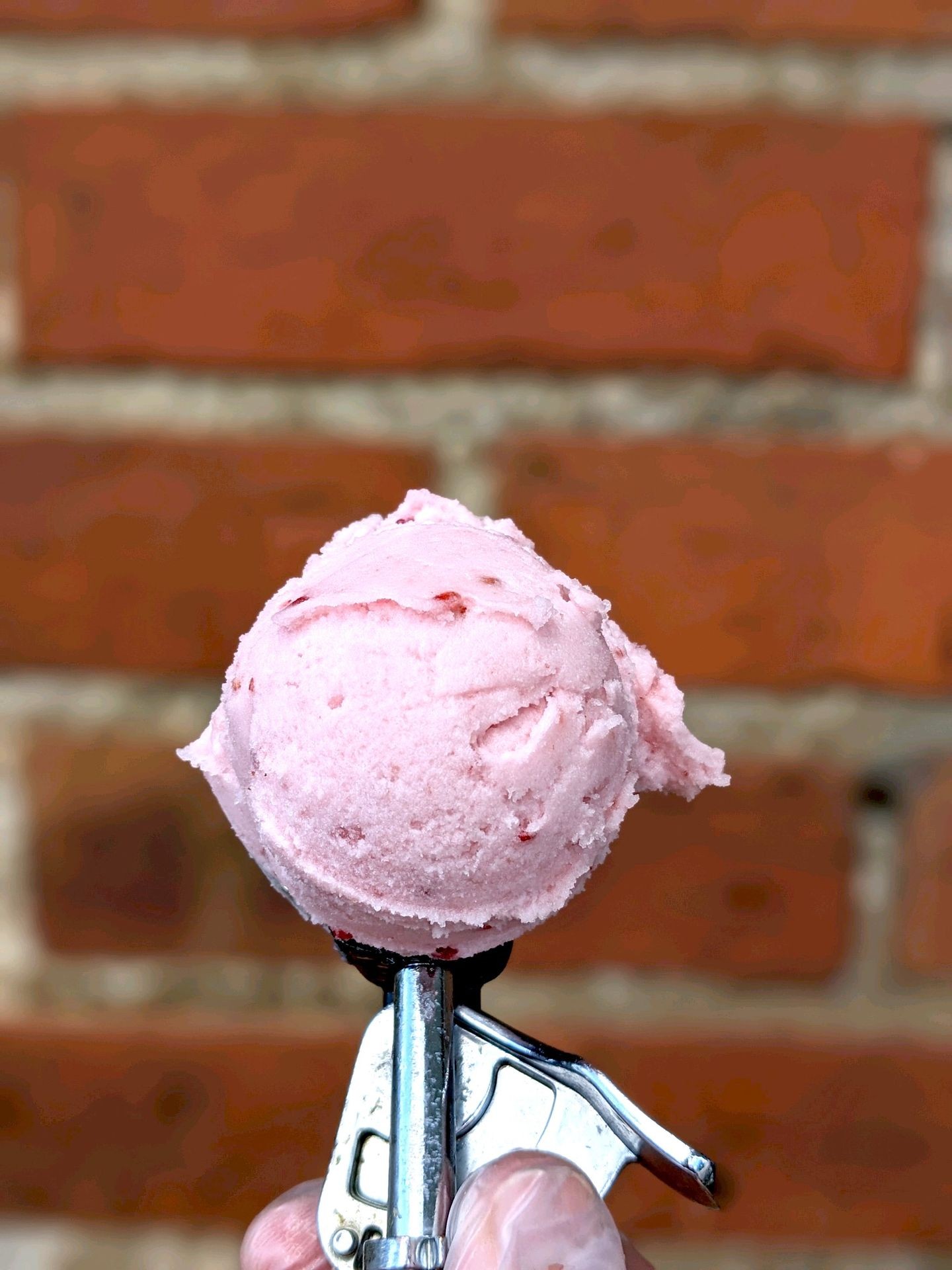 Close-up of a scoop of pink ice cream held against a brick wall background.