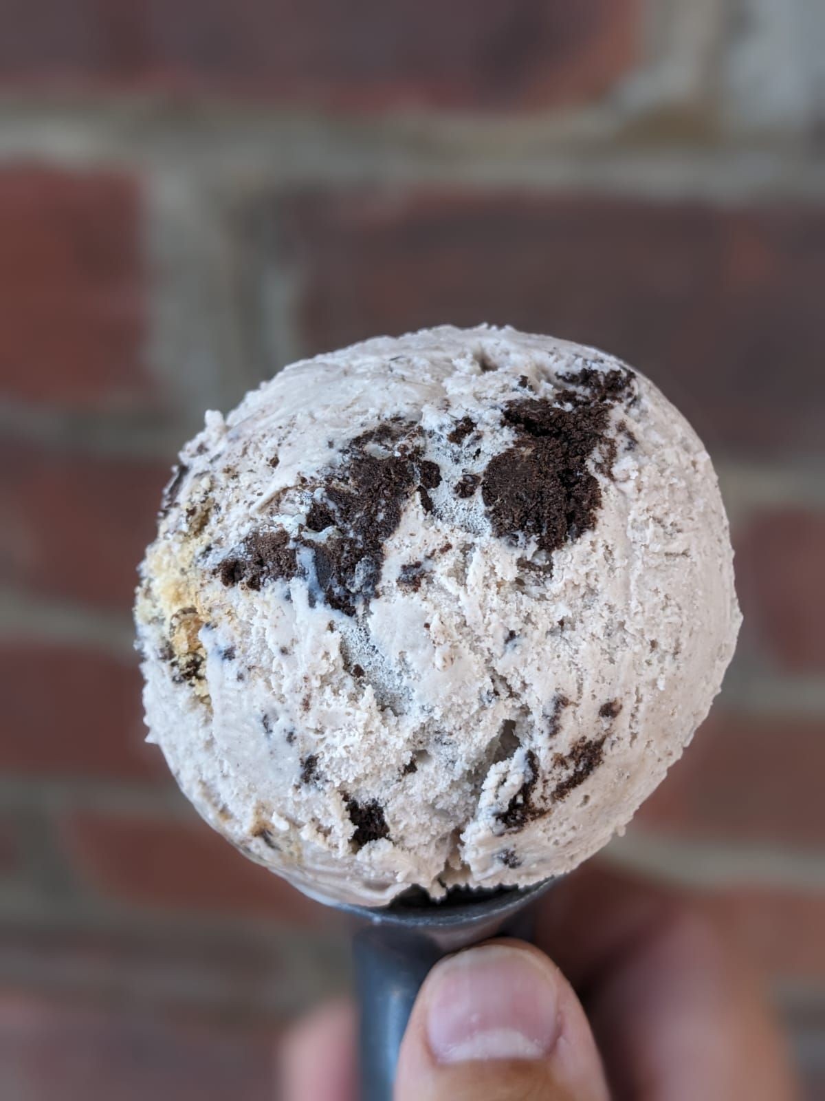 Close-up of a scoop of cookies and cream ice cream held against a blurred brick wall background.