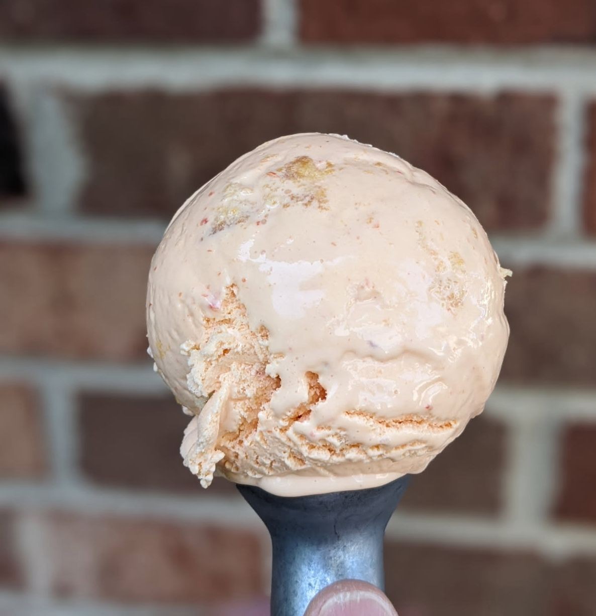 Close-up of a scoop of peach ice cream held against a blurred brick wall background.