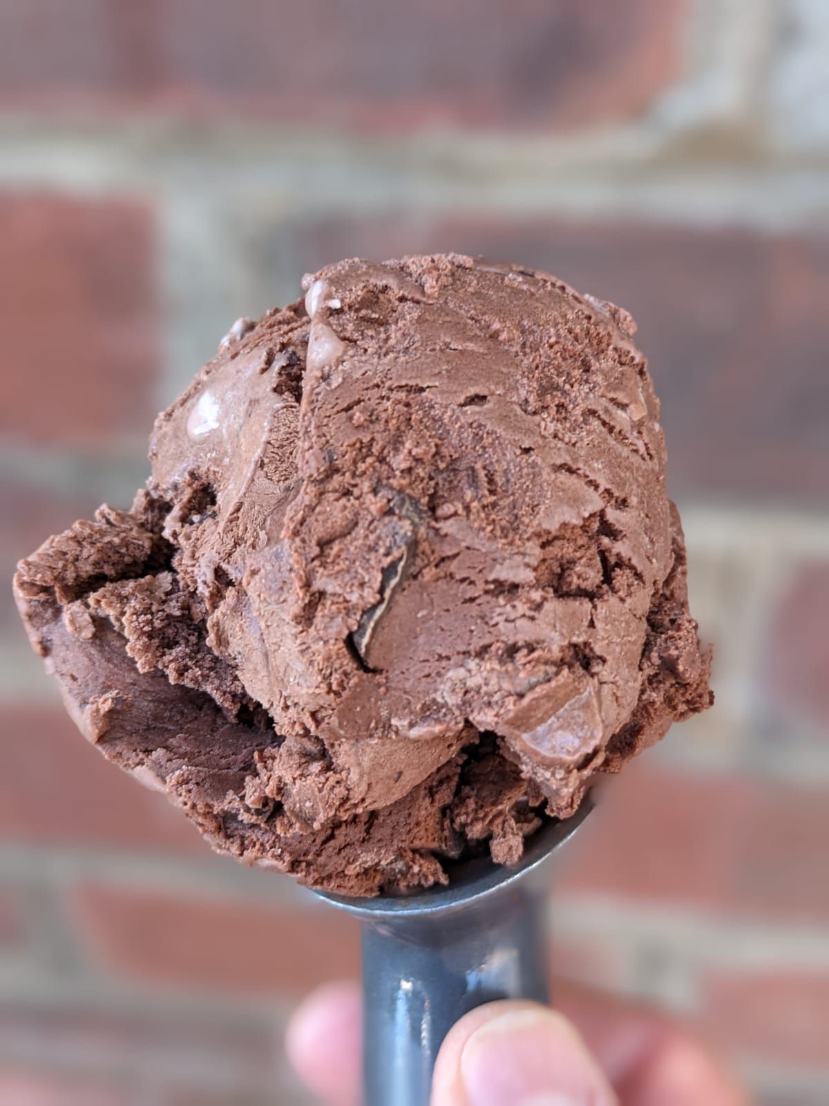 Close-up of a scoop of chocolate ice cream held against a blurred brick wall background.