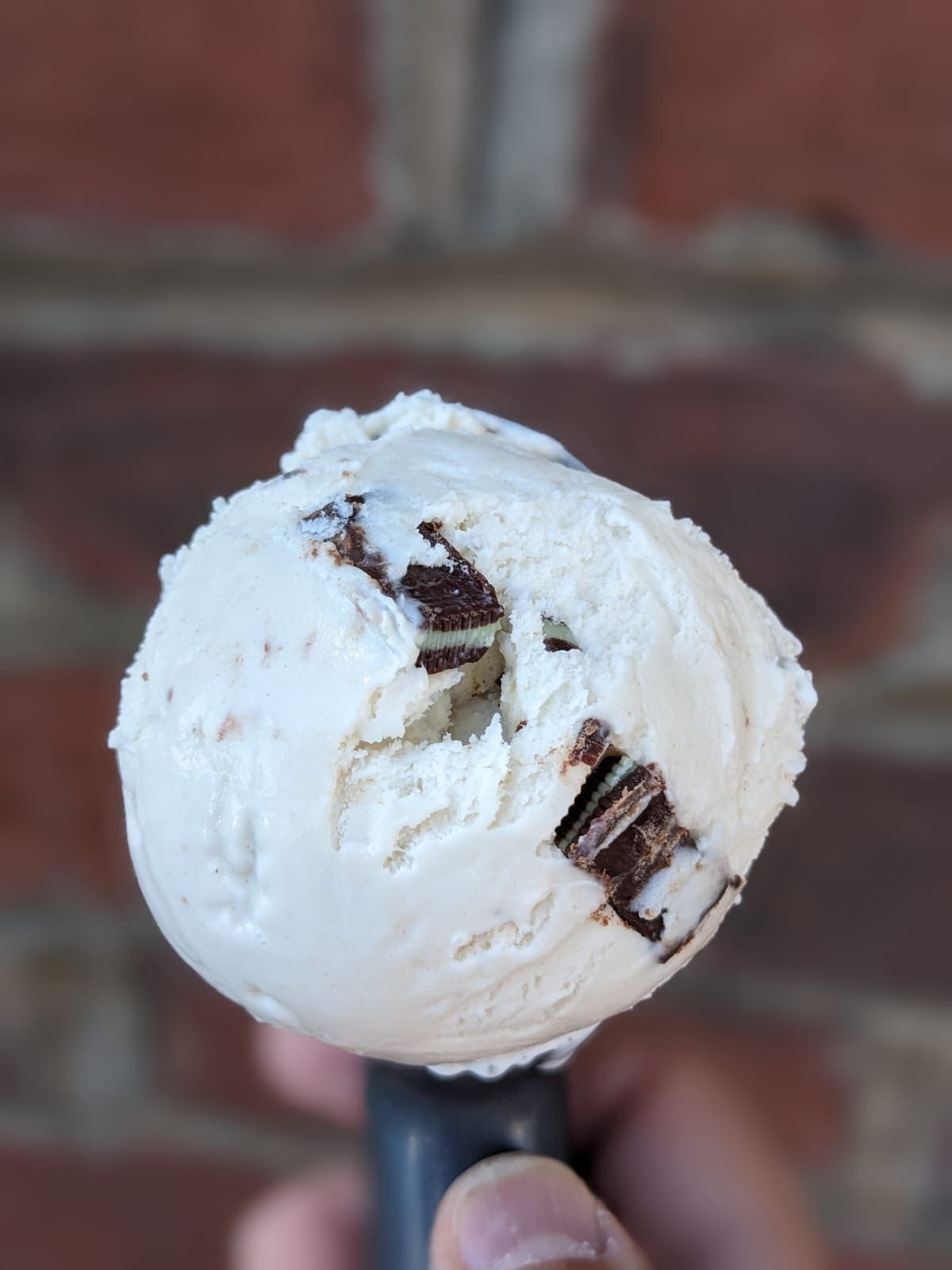 Close-up of a hand holding a scoop of cookies and cream ice cream against a blurred background.